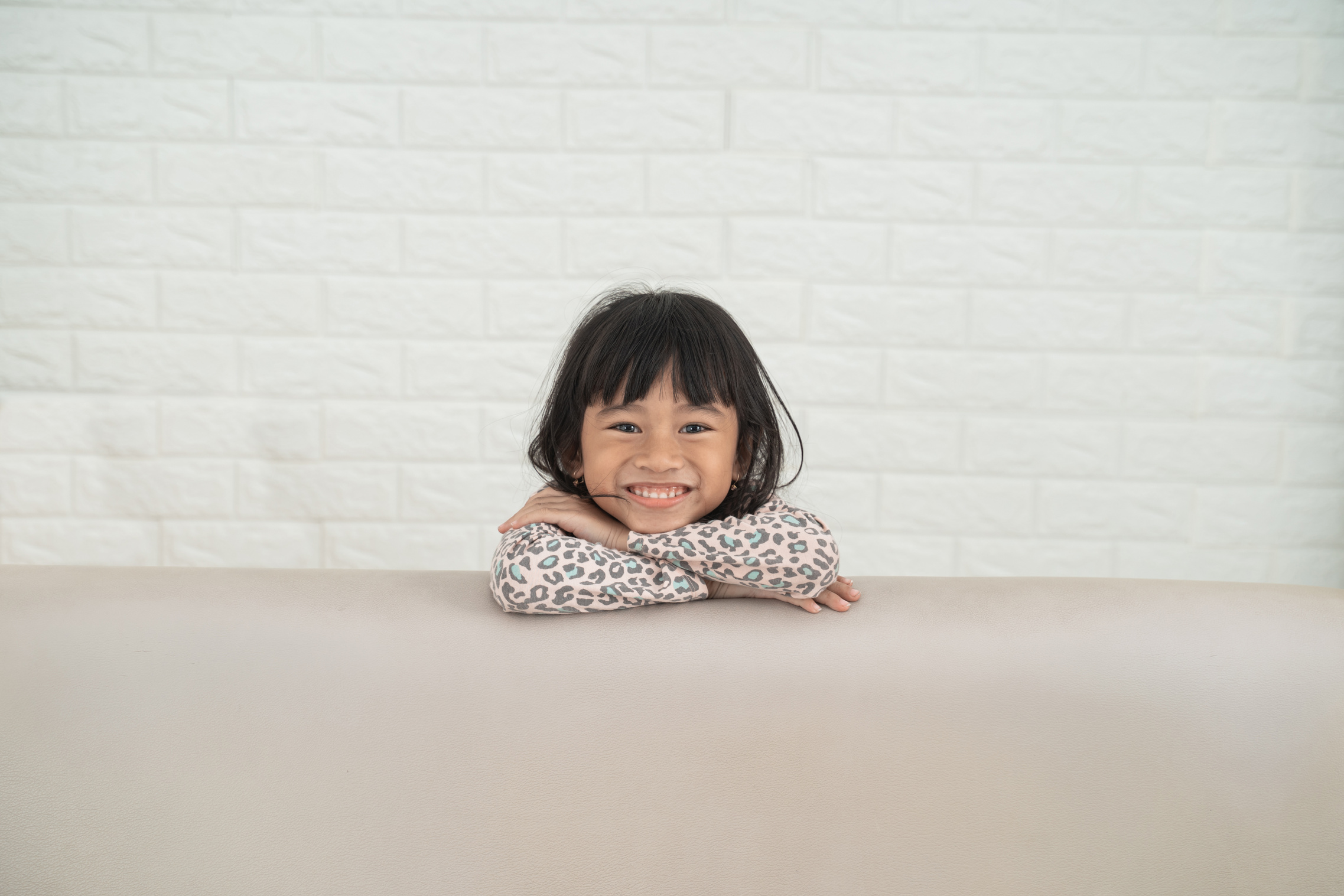 A young child smiling, resting their chin on their arms